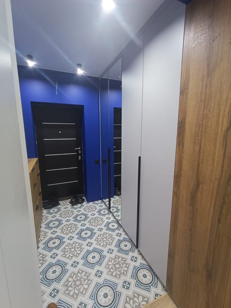 изайн современной прихожей с яркими синими стенами и узорчатой плиткой на полу. Встроенный шкаф-купе с зеркальным фасадом и вставками под дерево. Пример ремонта квартиры в [dynamic id="city" column="prepositional"]