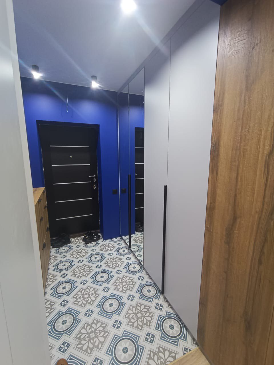 изайн современной прихожей с яркими синими стенами и узорчатой плиткой на полу. Встроенный шкаф-купе с зеркальным фасадом и вставками под дерево. Пример ремонта квартиры в [dynamic id="city" column="prepositional"]