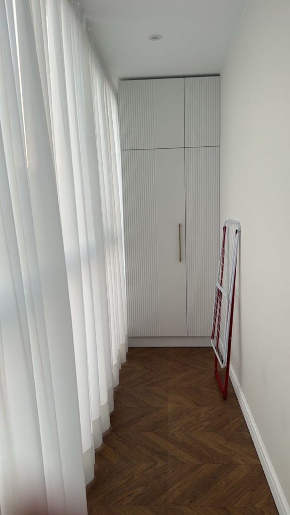 Встроенный шкаф до потолка с белыми рифлеными фасадами и золотыми ручками, установленный на лоджии с укладкой ламината "французская елка". Пример мебели на заказ в Томске.