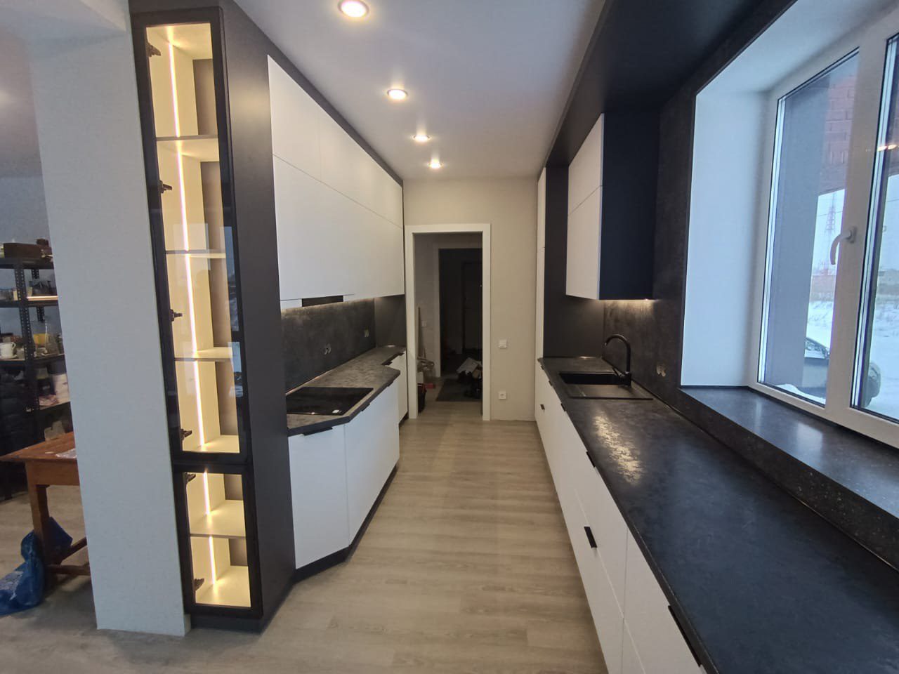 Современный дизайн прямой кухни: белые фасады без ручек, темная столешница переходящая в подоконник, и шкаф-витрина с подсветкой. Пример нашего ремонта кухни в г. Томск.